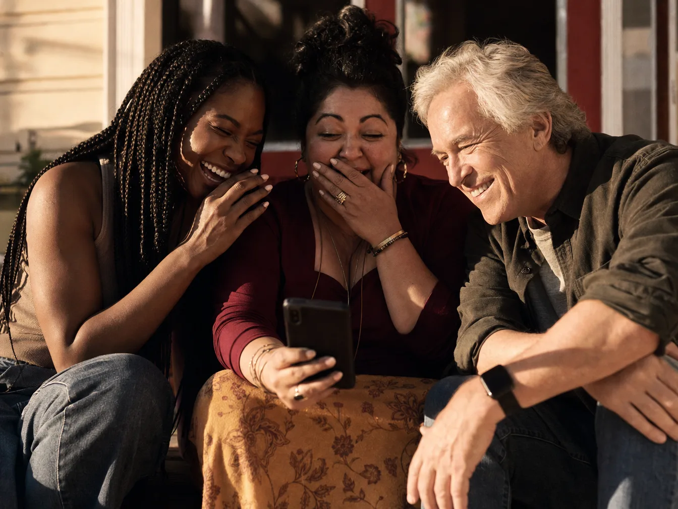 Three friends listening to a song together on a porch, cracking up