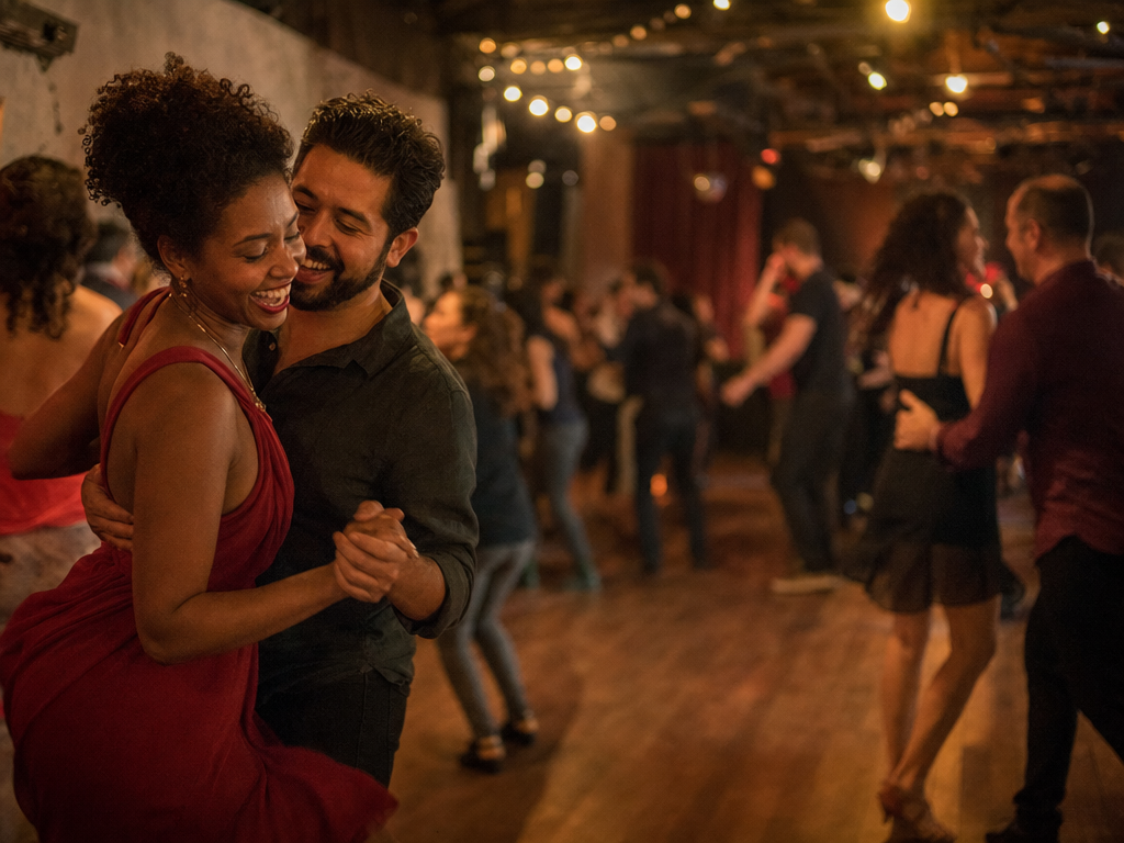 A couple laughing mid-dance at the salsa night where they met, the story behind a sample custom wedding song